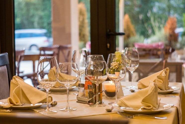 An elegant restaurant table by windows set for four with white plates and linens and tall wine glasses