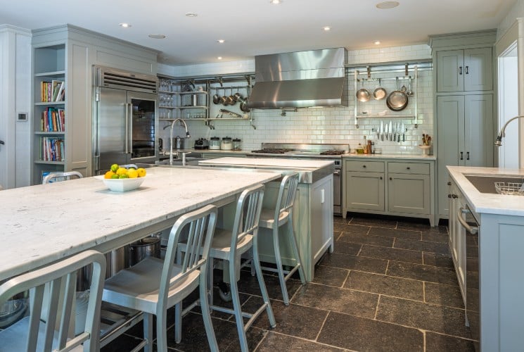 A large chef's kitchen with gas stove, hood, hanging pots and pans, island and large table with eight chairs