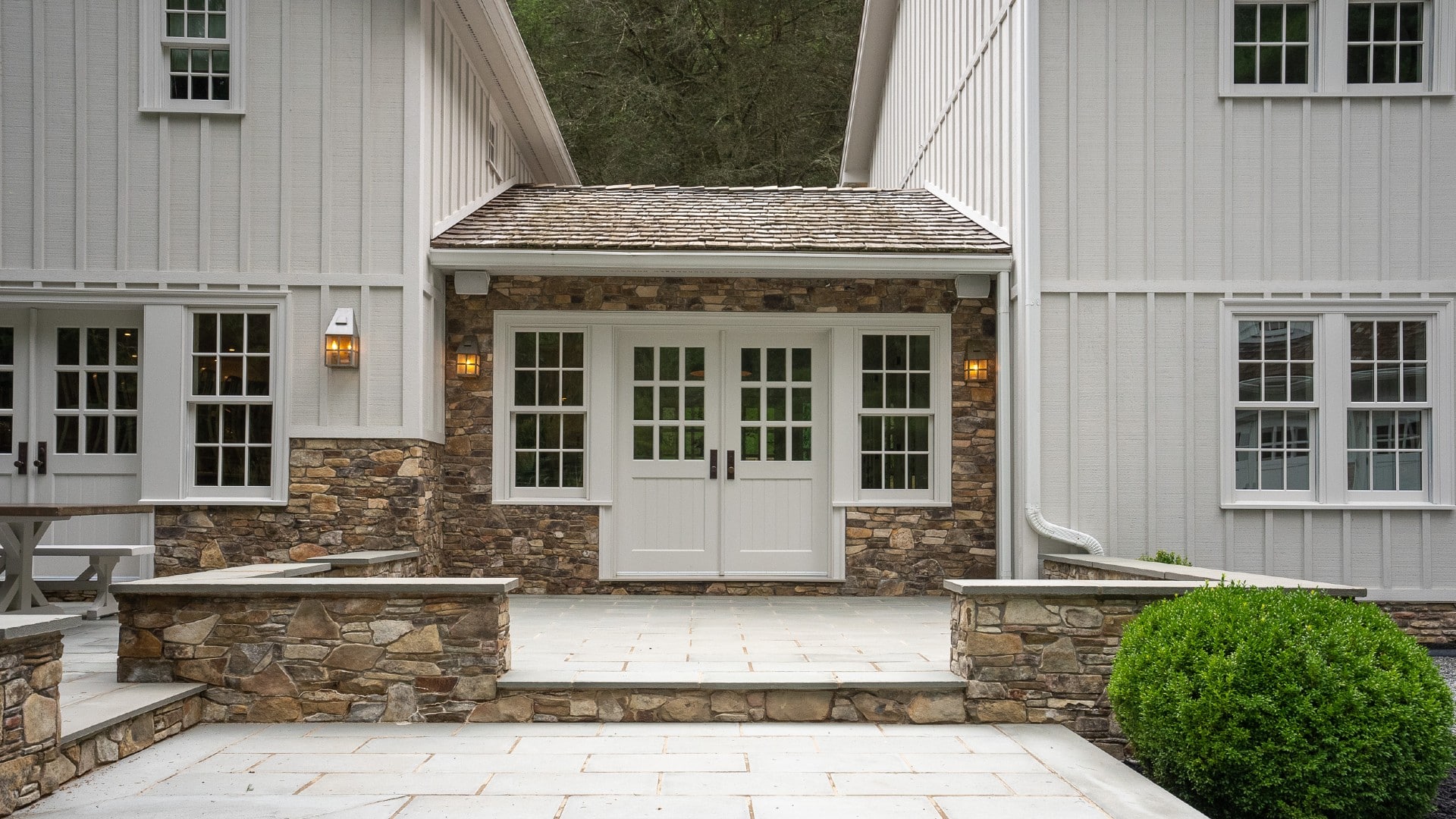 A portico walkway between two large areas of a white home with an expansive outdoor stone patio