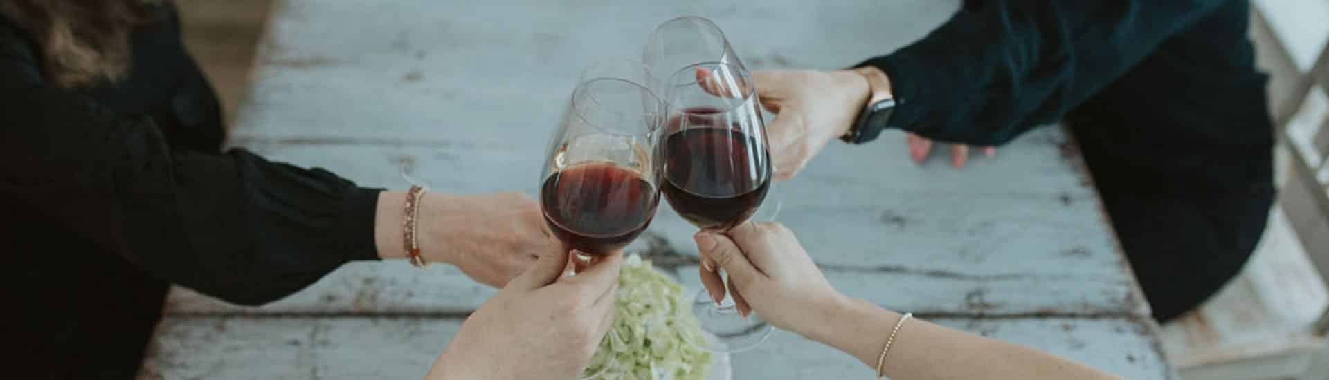 Four women sitting together each holding a glass of red wine at the center of the table