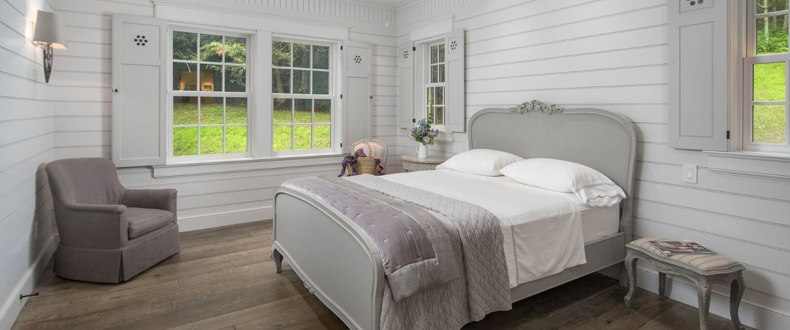 Bright and spacious bedroom with queen bed, sitting chairs, and large windows overlooking a green yard