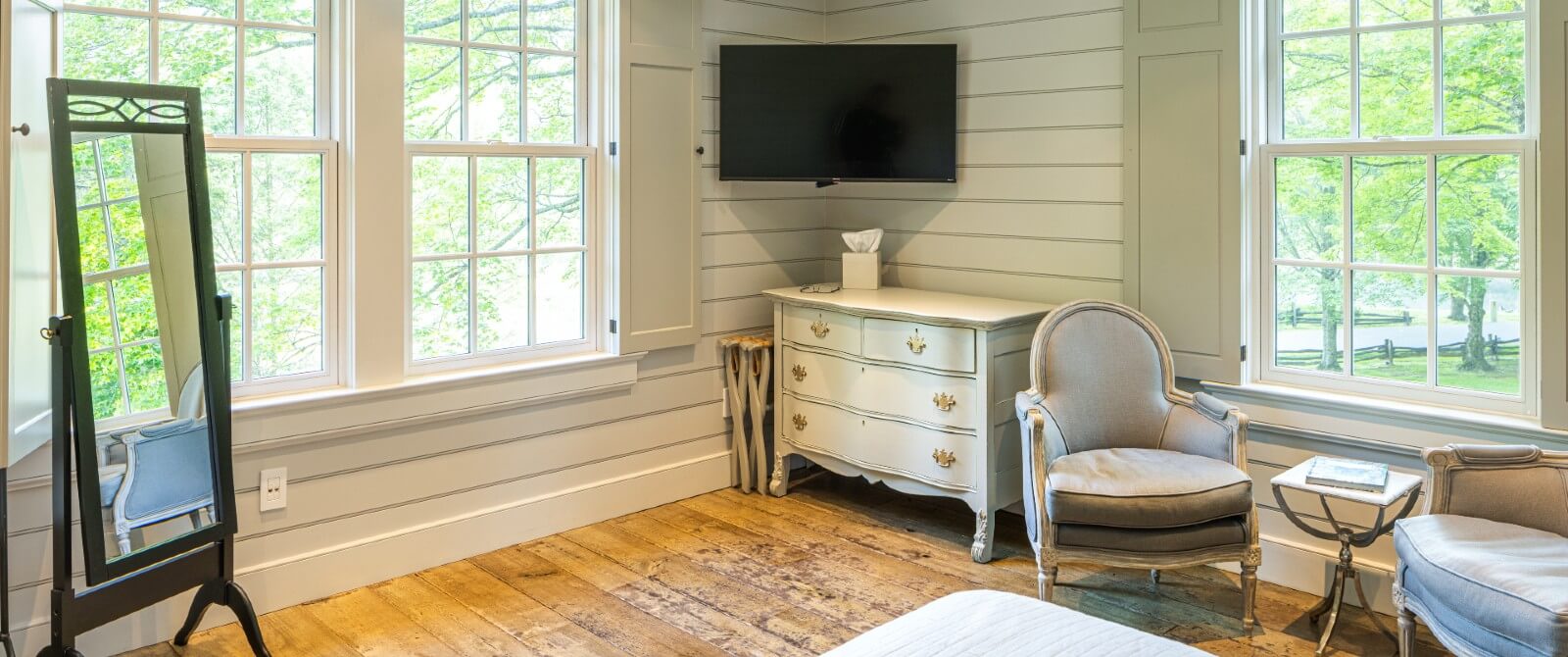 Bedroom with shiplap walls, standing mirror, two chairs and TV in corner over a dresser