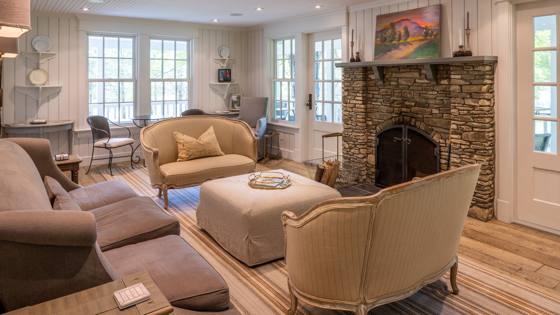 Living room with bright windows, shiplap walls and plush seating in front of a stone fireplace