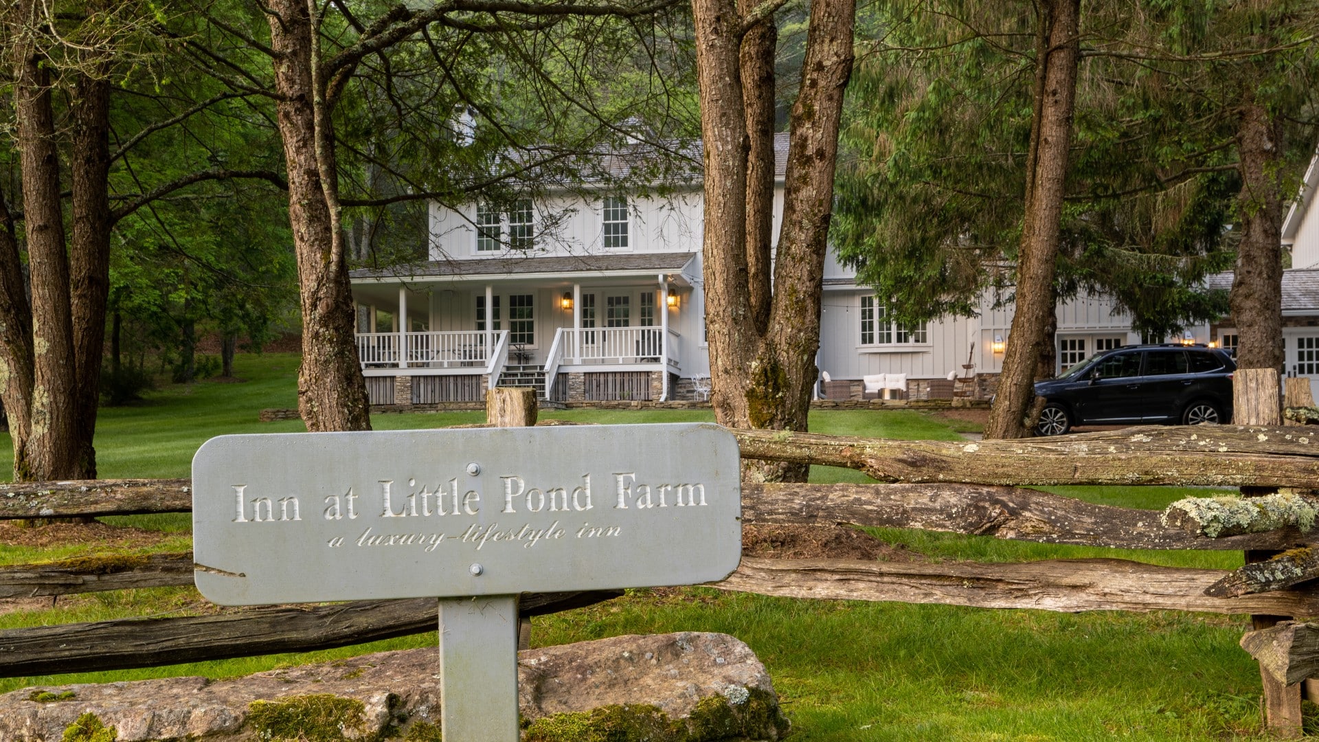 Rectangular sign for an inn by a wood fence with a large white home behind