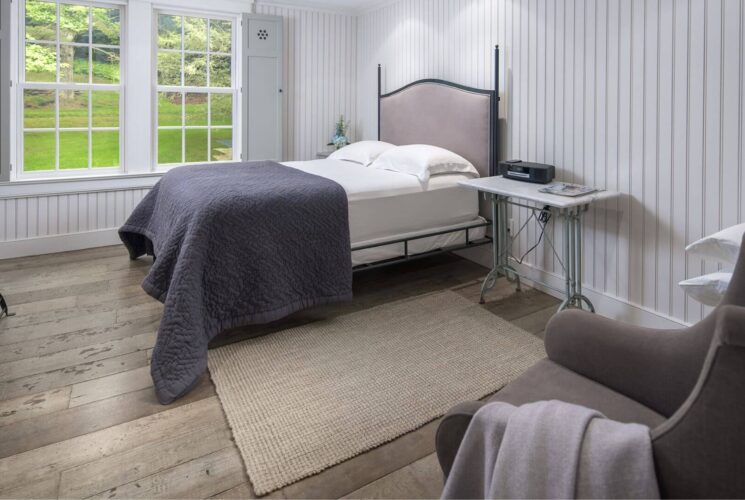 Beautiful bedroom with shiplap walls, queen bed, plush sitting chair and bright window with shutters