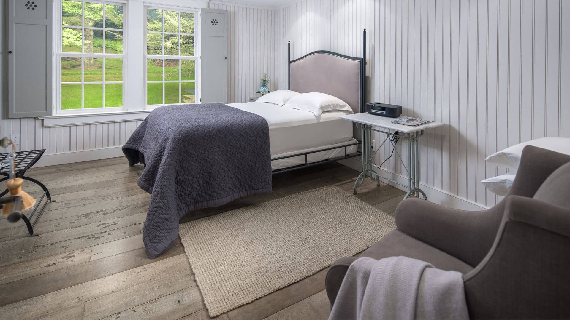 Beautiful bedroom with shiplap walls, queen bed, plush sitting chair and bright window with shutters