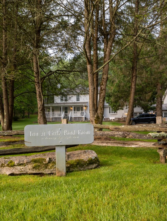 Rectangular sign for an inn by a wood fence with a large white home behind