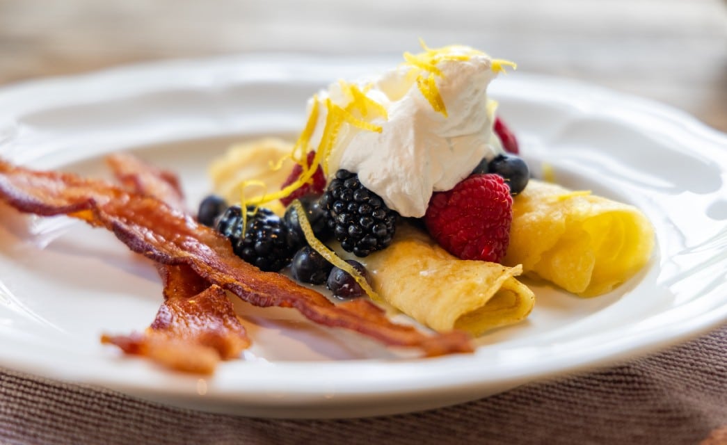 Golden crepes with berries, whipped cream, lemon zest and two strips of bacon