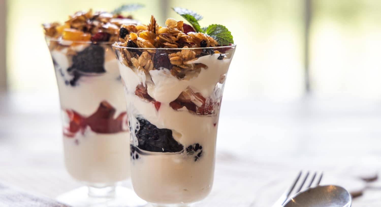 Two glass parfaits cups of yogurt, berries, granola and sprig of mint